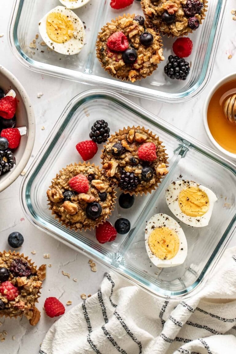 Overhead view of two glass meal prep containers filled with mixed berry oatmeal cups and sliced hard boiled eggs.