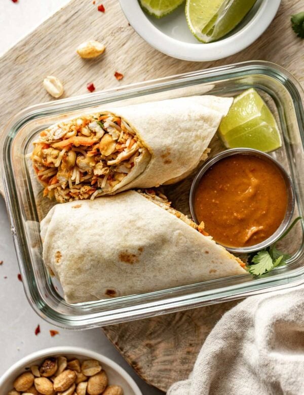 Overhead view of a peanut chicken wrap cut in half placed in a meal prep container