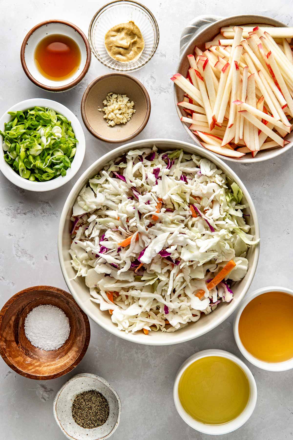 Overhead view of a variety of ingredients for Apple Slaw in different sized bowls. 