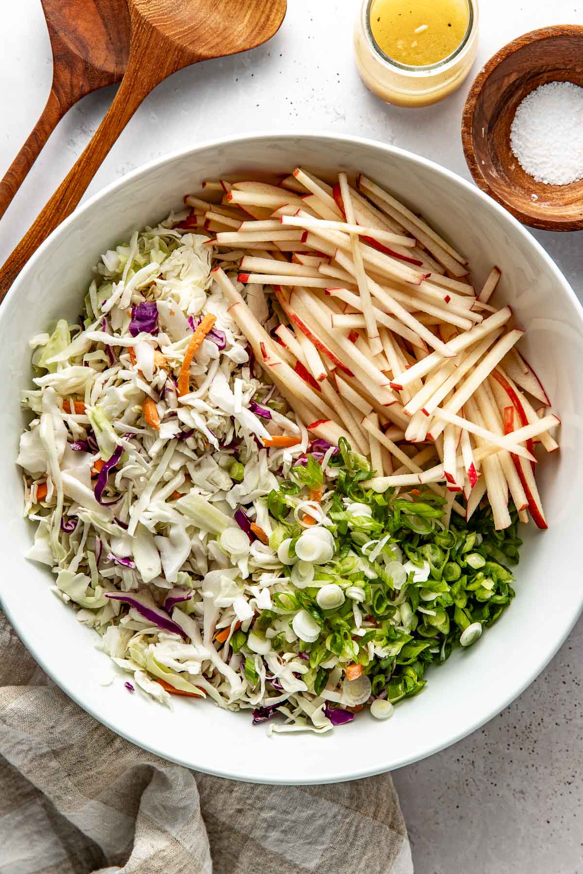 Overhead view of a white bowl filled with Apple Slaw ingredients in different sections of the bowl. 