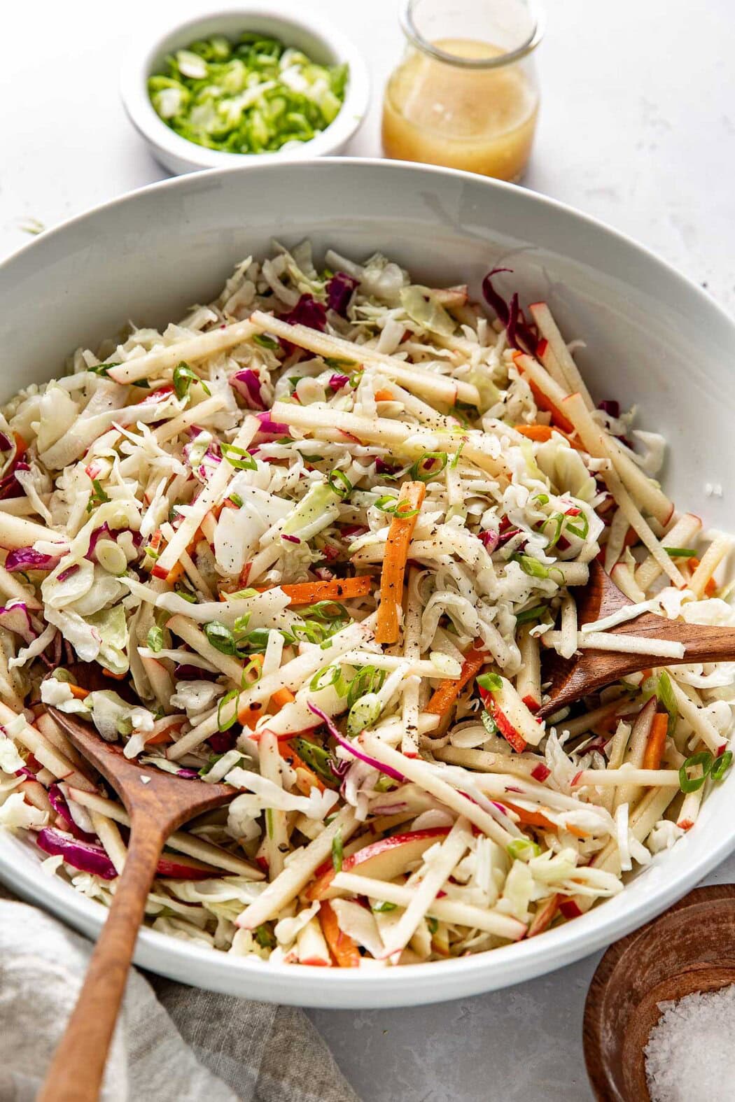 Close up view of a white bowl filled with colorful Apple Slaw topped with black pepper and green onions. 