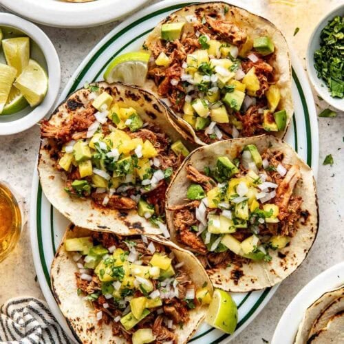 Overhead view of a plate filled with Crockpot Tacos Al Pastor in tortillas topped with fresh pineapple and cilantro.