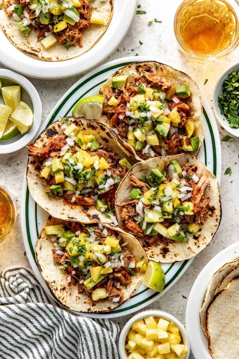 Overhead view of a platter filled with four tortillas filled with tacos al pastor topped with fresh pineapple and cilantro. 