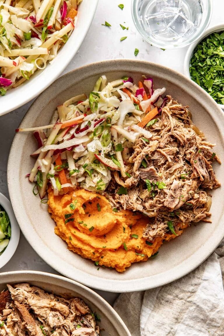 Overhead view of an apple cider pork bowl topped with apple slaw and mashed sweet potatoes. 