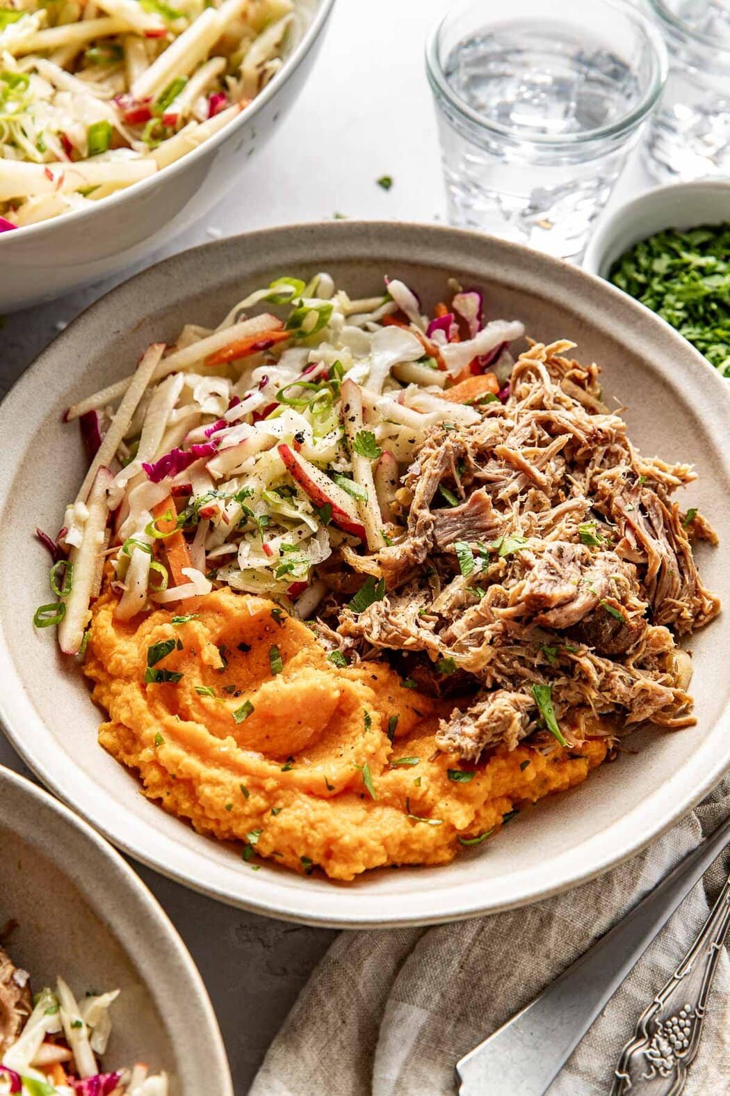 Close up view of a bowl of Mashed Sweet Potatoes with pulled pork and apple slaw on the side. 