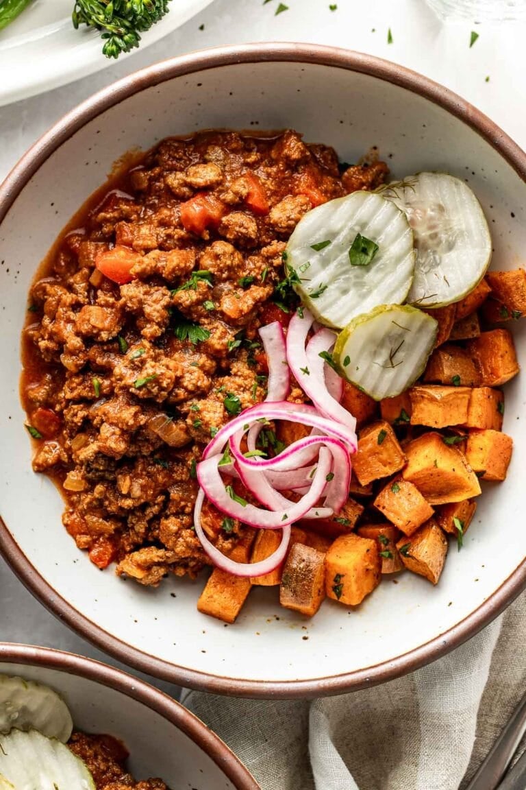 Overhead view of a bowl filled with sloppy joe meat on top of roasted sweet potatoes and topped with red pickled onions and crispy dill pickles. 