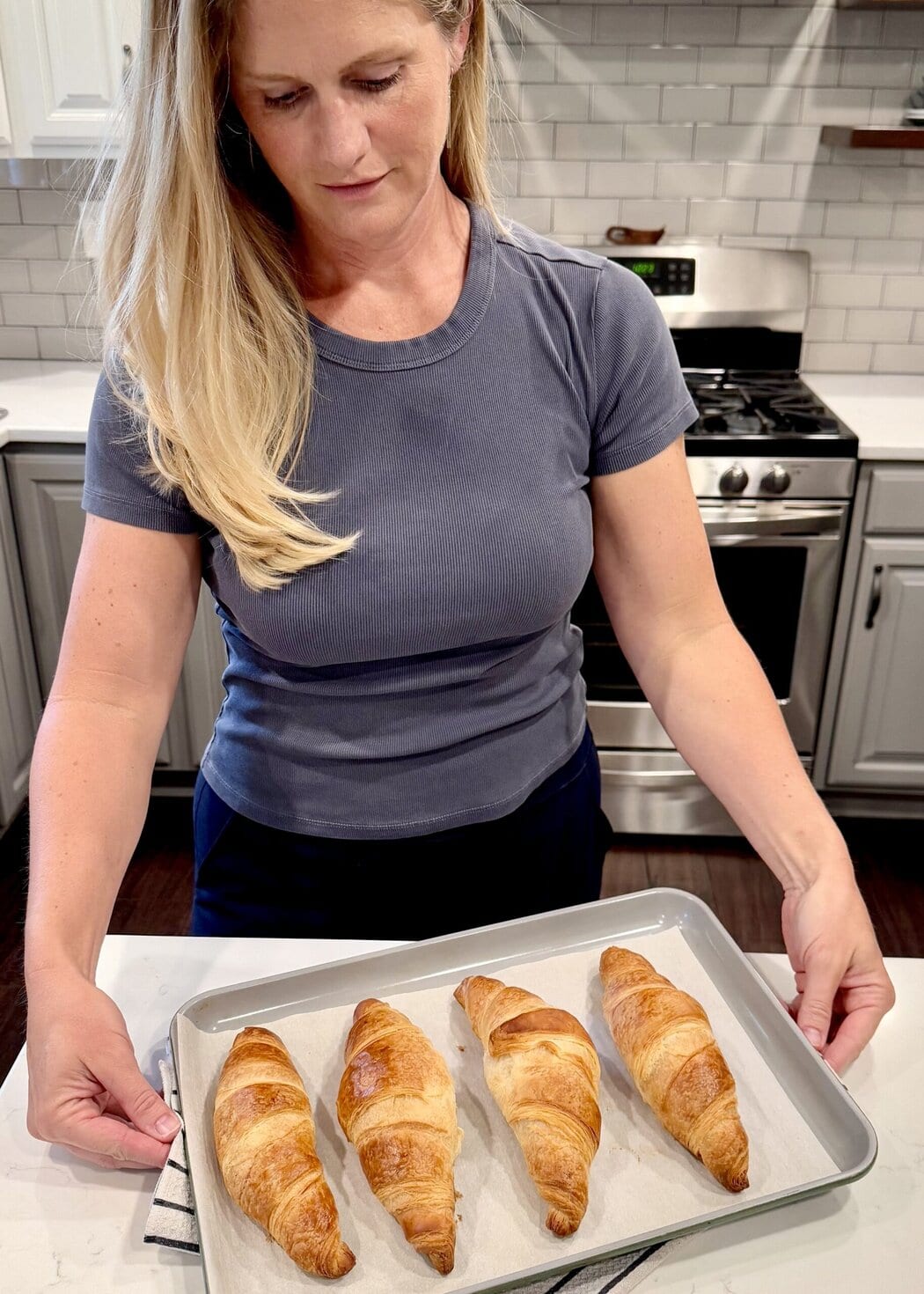 Close up view of a woman setting a pan of baked croissants on the counter.