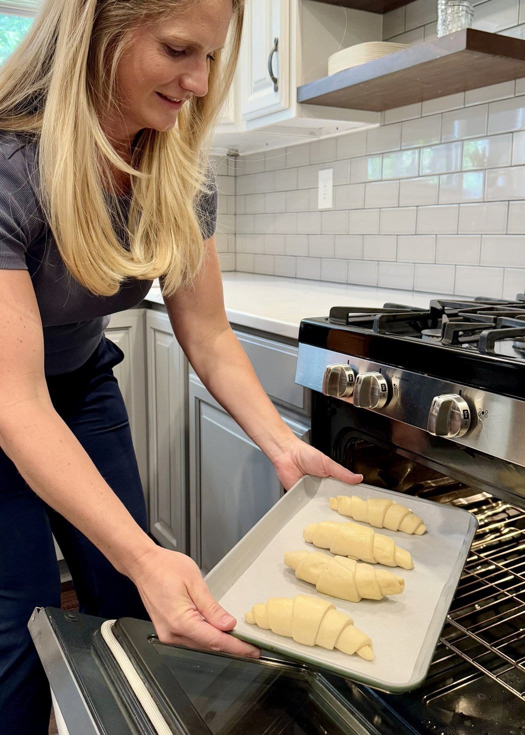 Close up view of a woman in a kitchen putting a pan of frozen croissants in an oven.