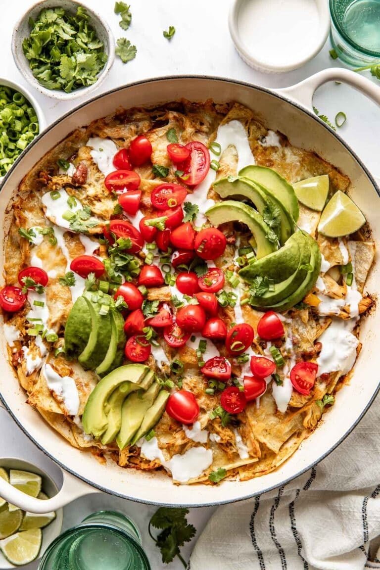 Overhead view of a skillet filled with chicken enchiladas topped with sliced avocado and diced tomatoes.