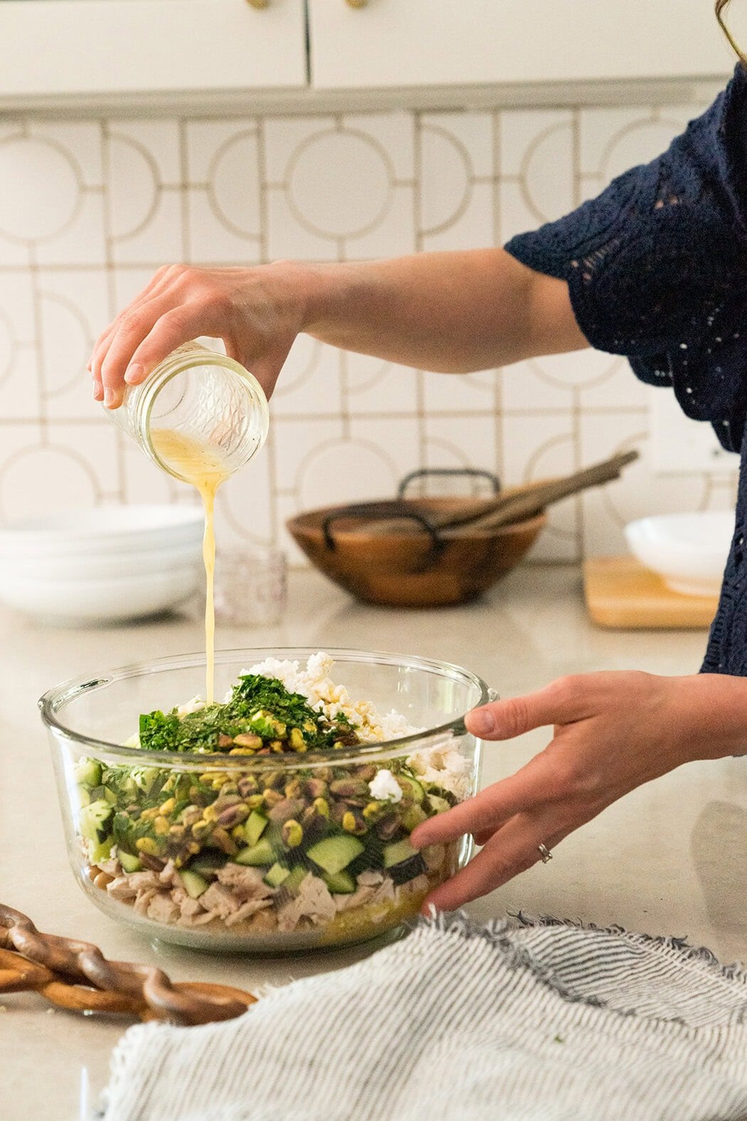 Close up view of a woman pouring a lemon vinaigrette over a salad in a glass bowl.