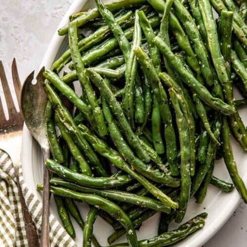 Overhead view of a platter filled with freshly roasted green beans topped with sat and pepper and garnished with lemon.
