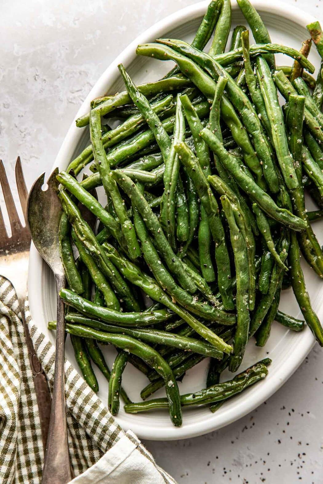 Close up view of a platter filled with freshly roasted green beans topped with salt and pepper. 