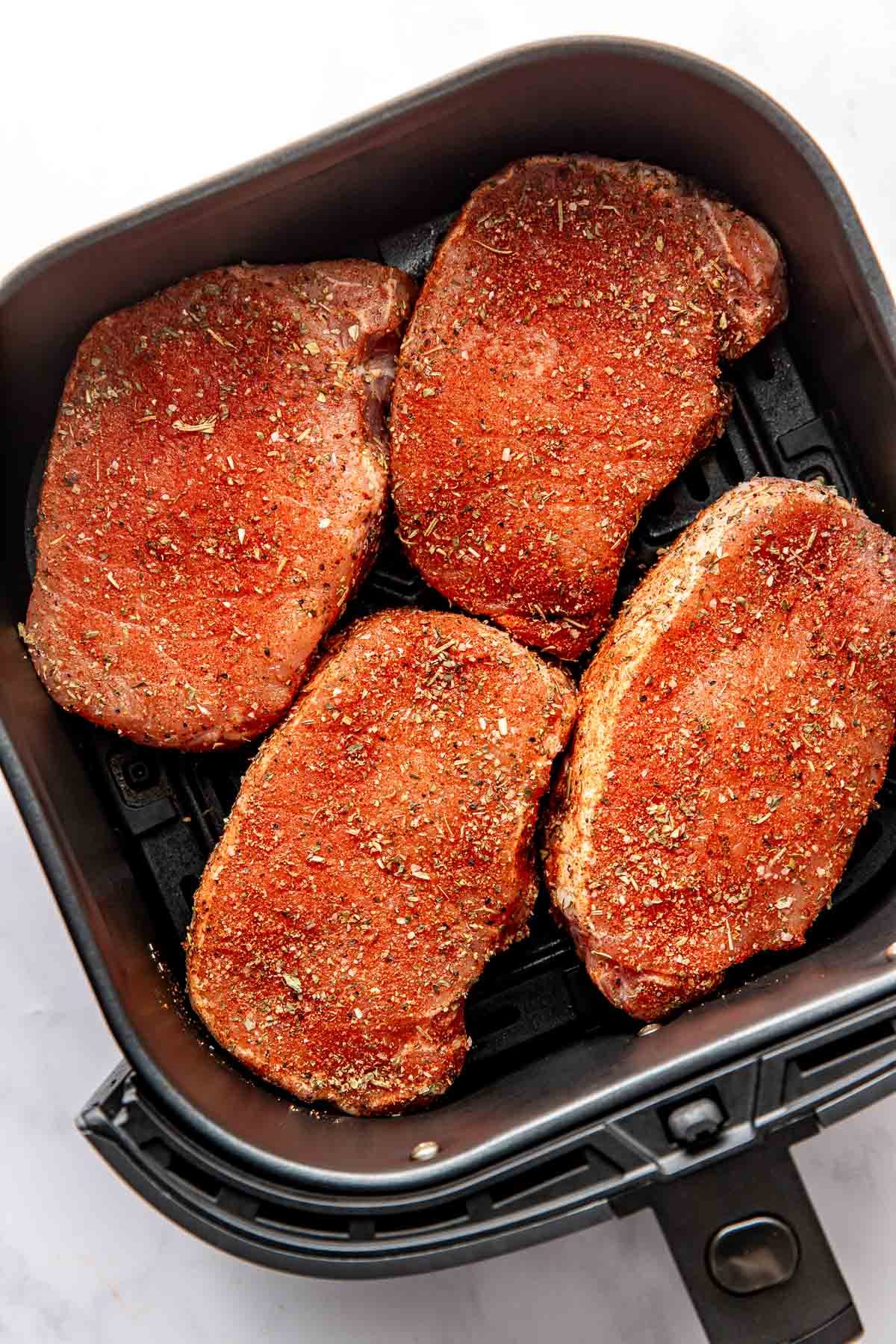 Overhead view of four perfectly seasoned pork chops in an air fryer basket ready for cooking. 