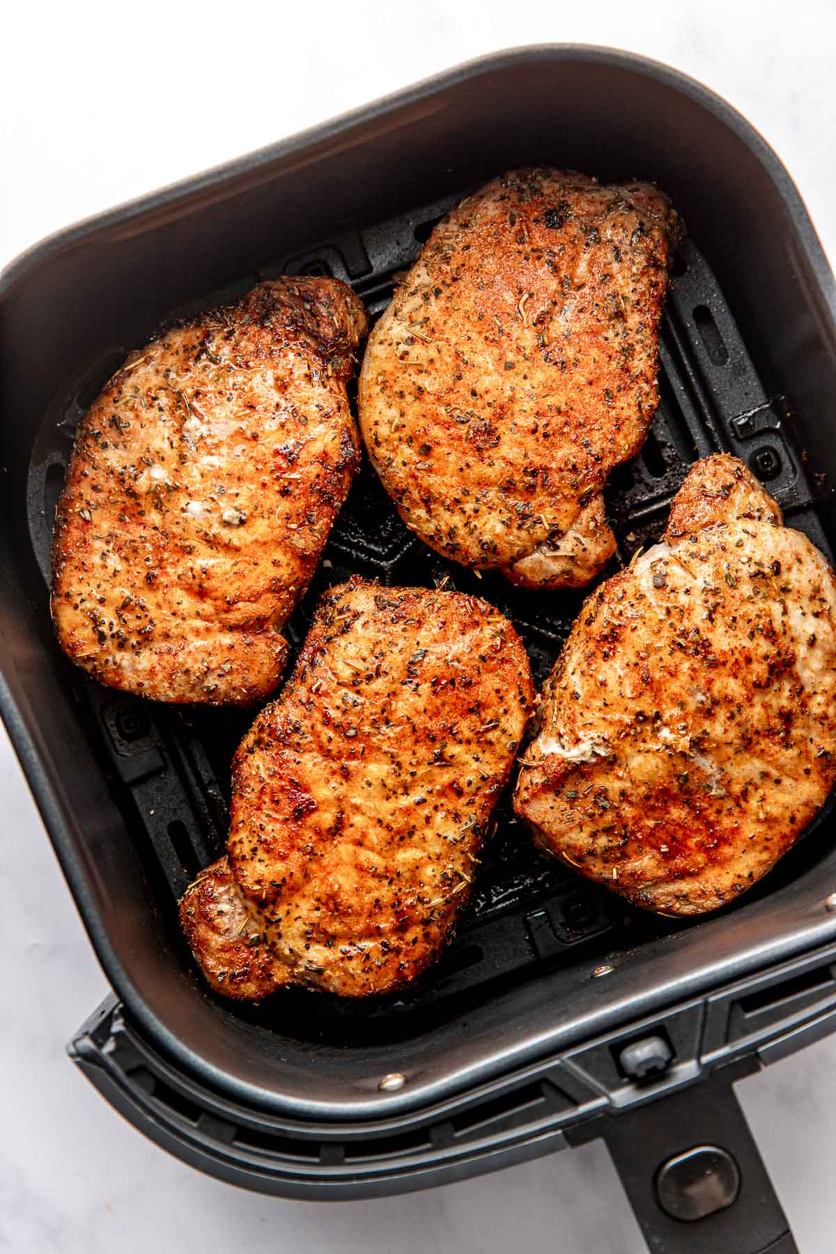 Overhead view of an air fryer basket filled with four freshly fried pork chops. 