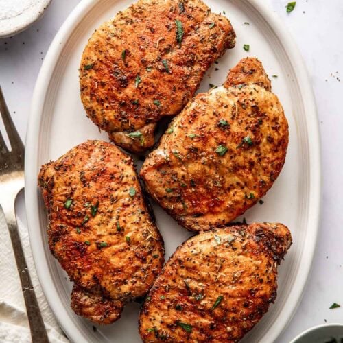 Close up view of a platter filled with four freshly fried pork chops perfectly seasoned and crisp on the edges.
