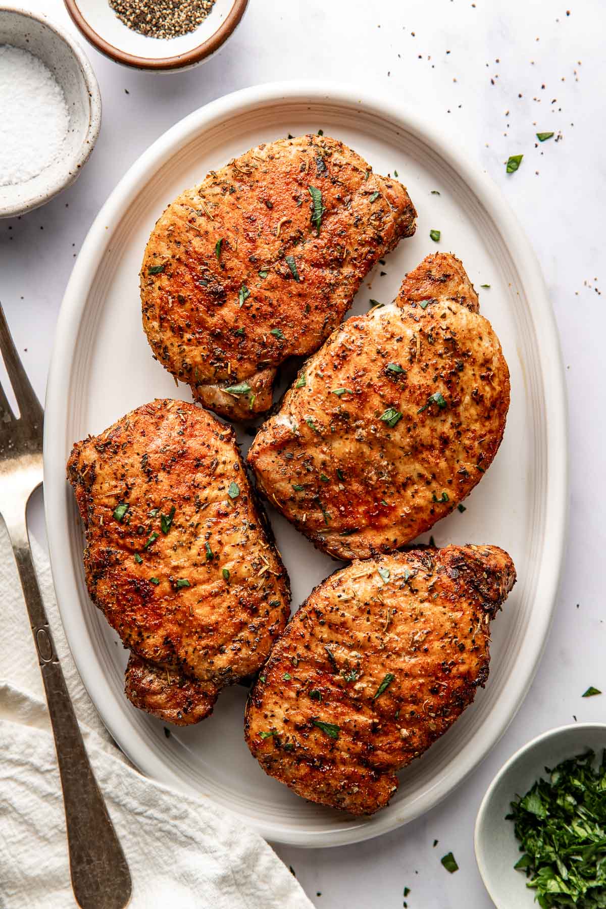 Overhead view of a platter filled with four perfectly crisp air fried pork chops topped with seasonings and herbs. 