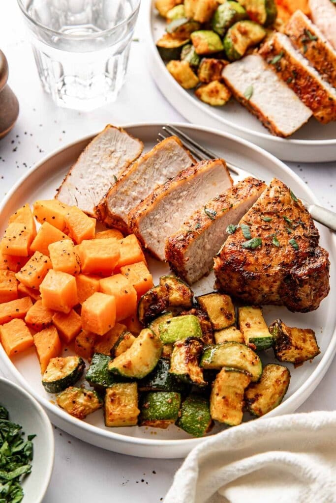 Close up view of a plate filled with freshly fried and sliced air fryer porkchops next to cubed butternut squash and crisp zucchini. 