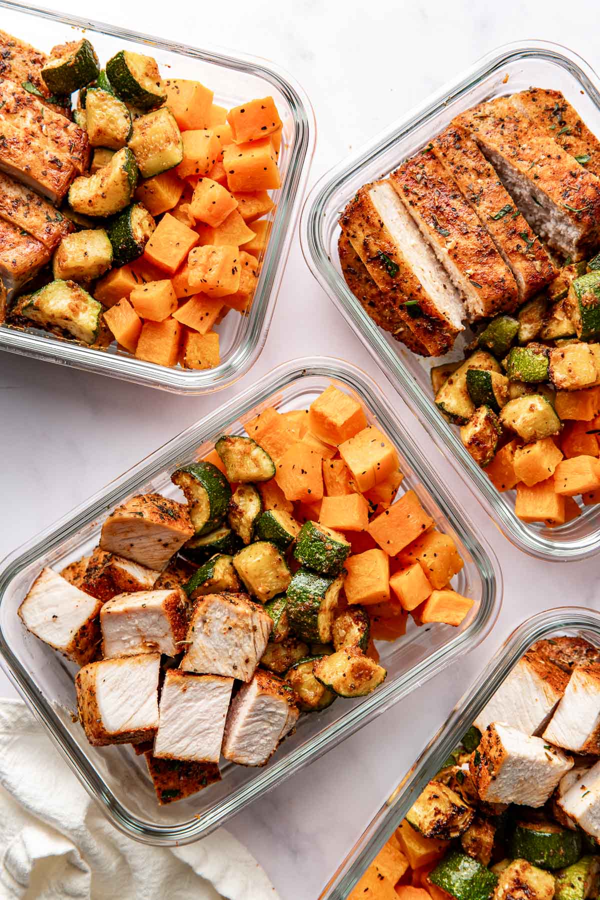 Overhead view of glass meal prep containers filled with sliced pork chops, zucchini, and butternut squash. 