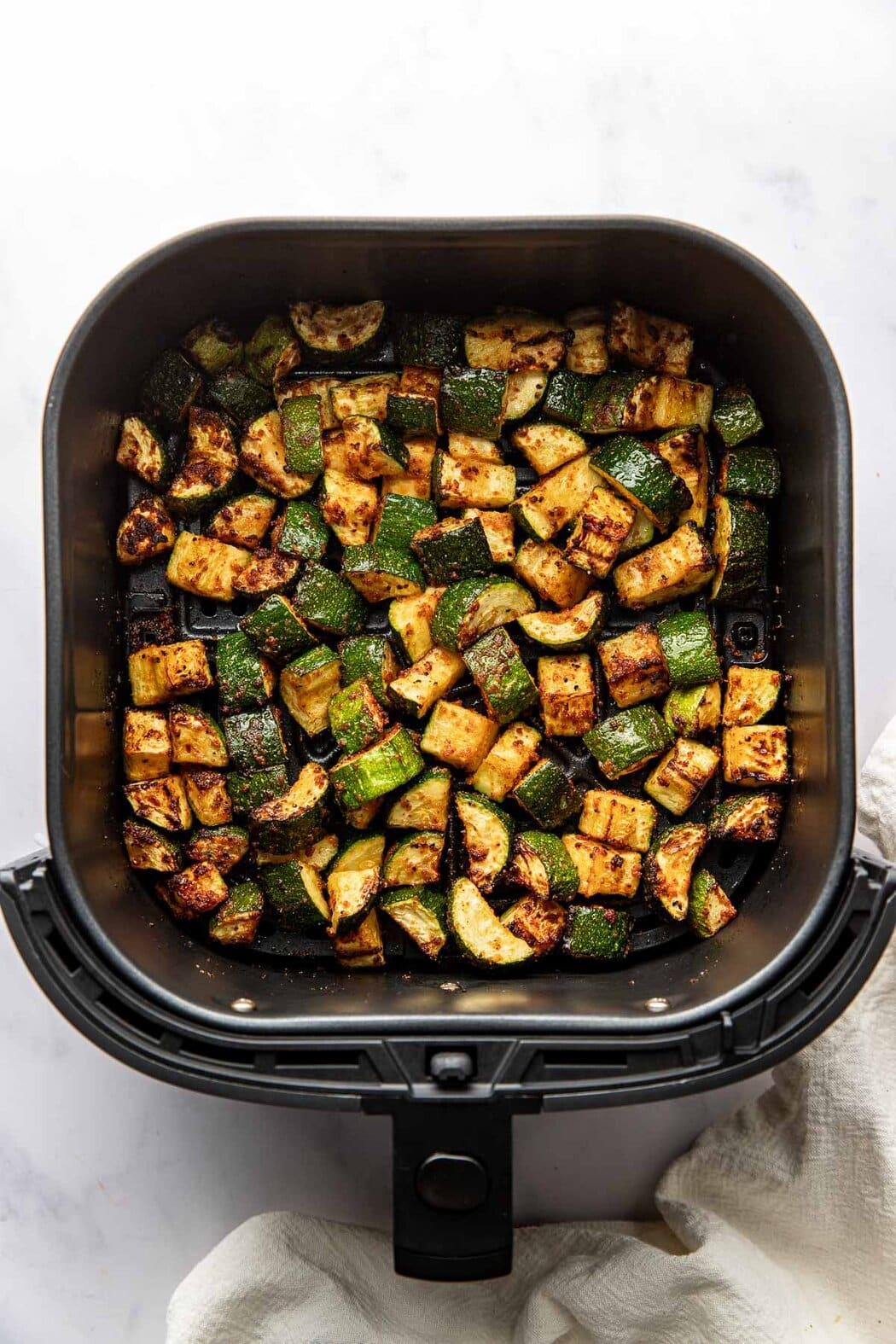 Overhead view of an air fryer basket filled with freshly roasted zucchini showing the crisp outside texture. 
