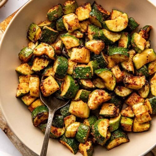Overhead view of a ceramic bowl filled with crisp Air Fryer Zucchini pieces with a spoon in the bowl.