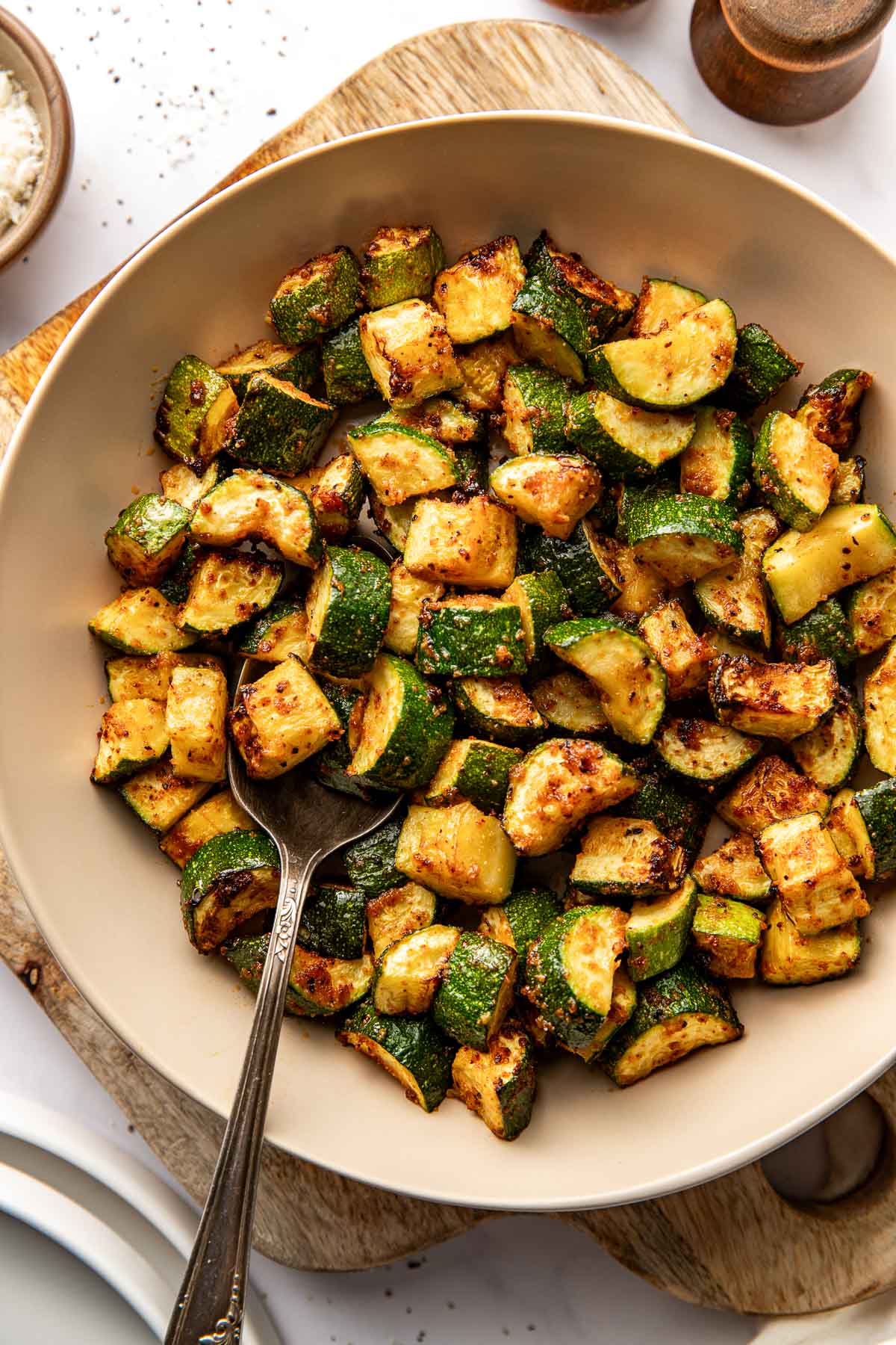 Overhead view of a ceramic bowl filled with Air Fryer Zucchini pieces with crisp texture. 