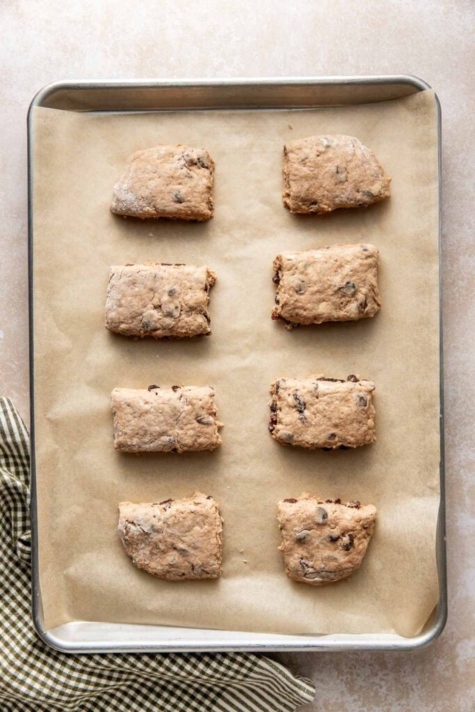 Eight unbaked cinnamon raisin biscuits on a parchment paper line baking sheets.
