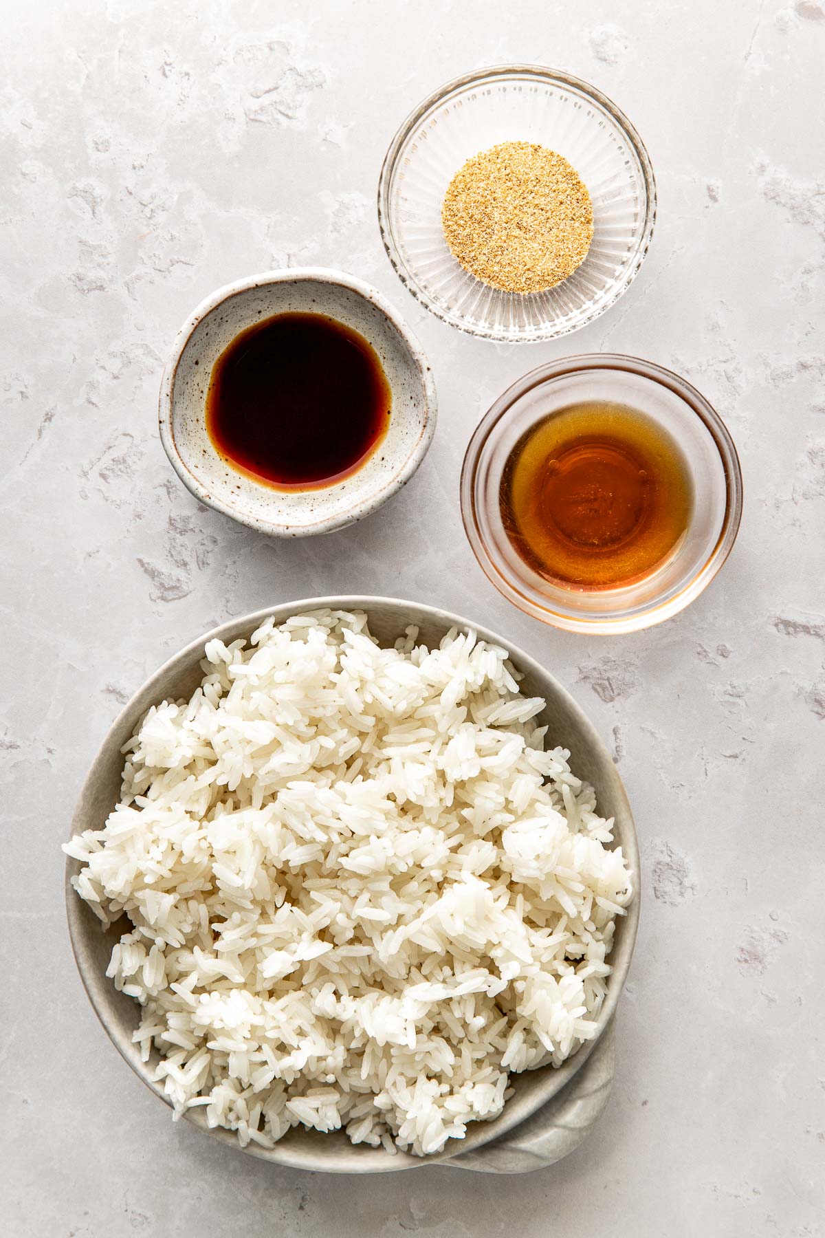 Overhead view of a variety of ingredients for Sheet Pan Crispy Rice in different sized bowls on a marble countertop.