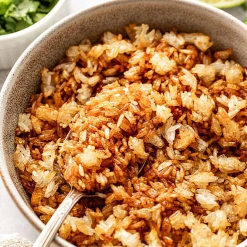 Close up view of a bowl filled with crispy roasted rice with a spoon in the bowl.