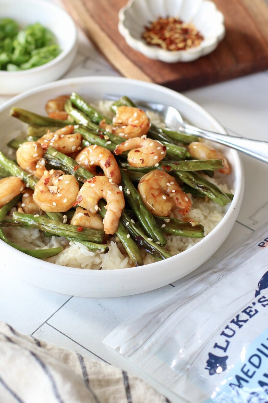 A shallow white bowl of rice and honey garlic shrimp with a package of Luke's Lobster frozen shrimp in the foreground. 