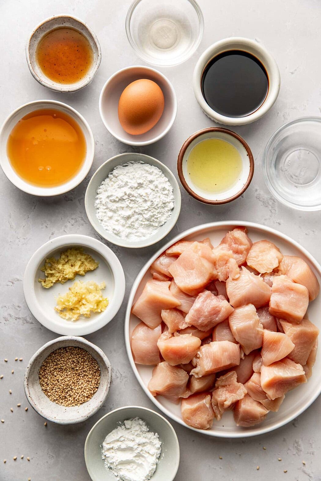 Overhead view of a variety of ingredients for Sesame Chicken in different sized bowls. 