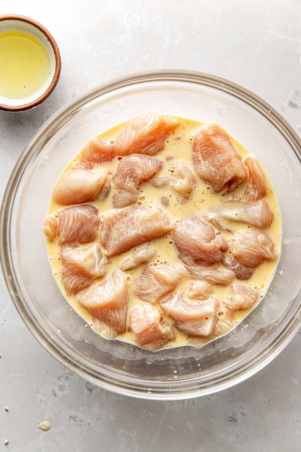 Overhead view of a glass bowl filled with chicken marinating in an egg mixture. 