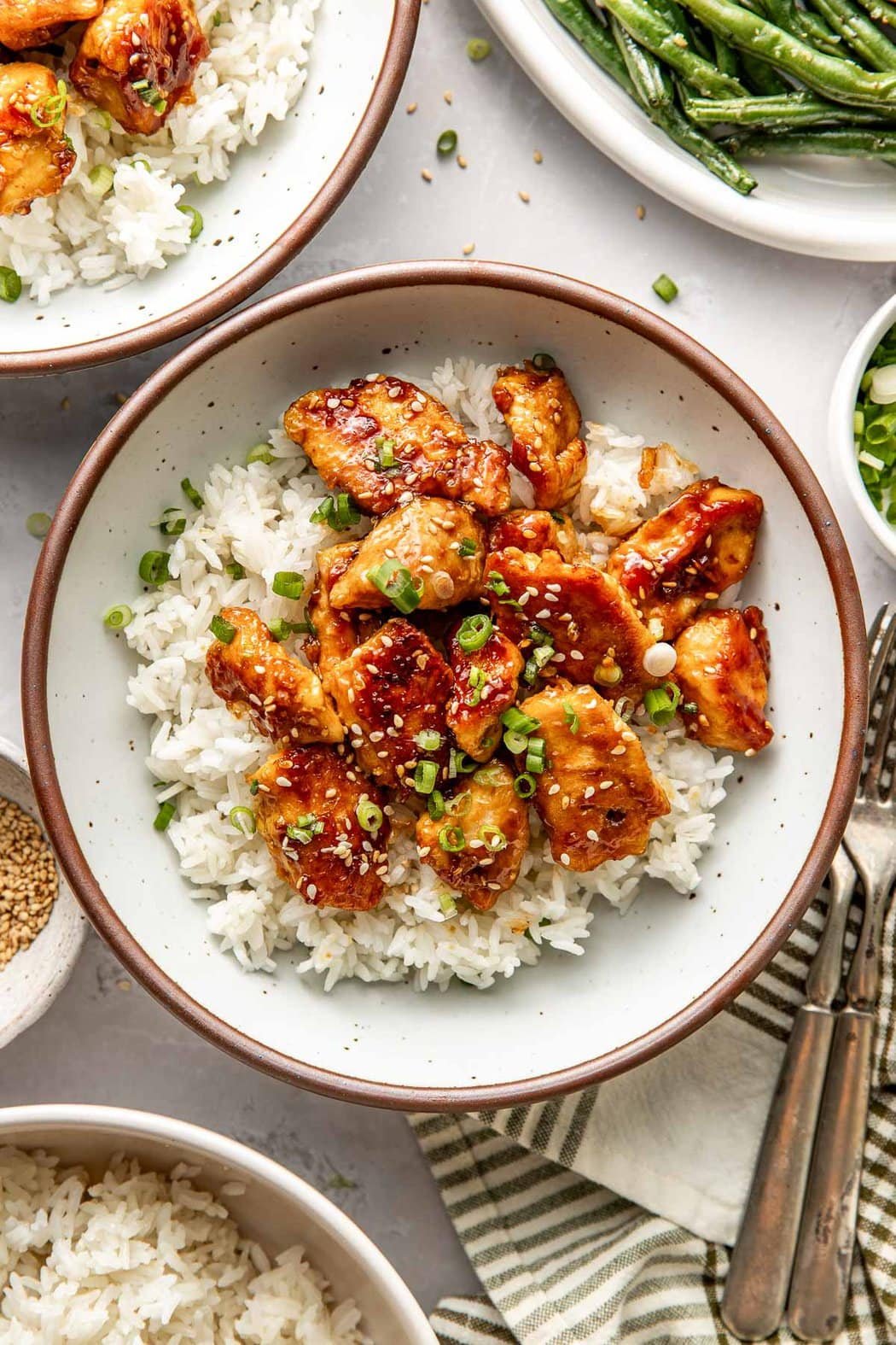Overhead view of a plate of white rice topped with sesame chicken pieces topped with sesame seeds and green onions. 