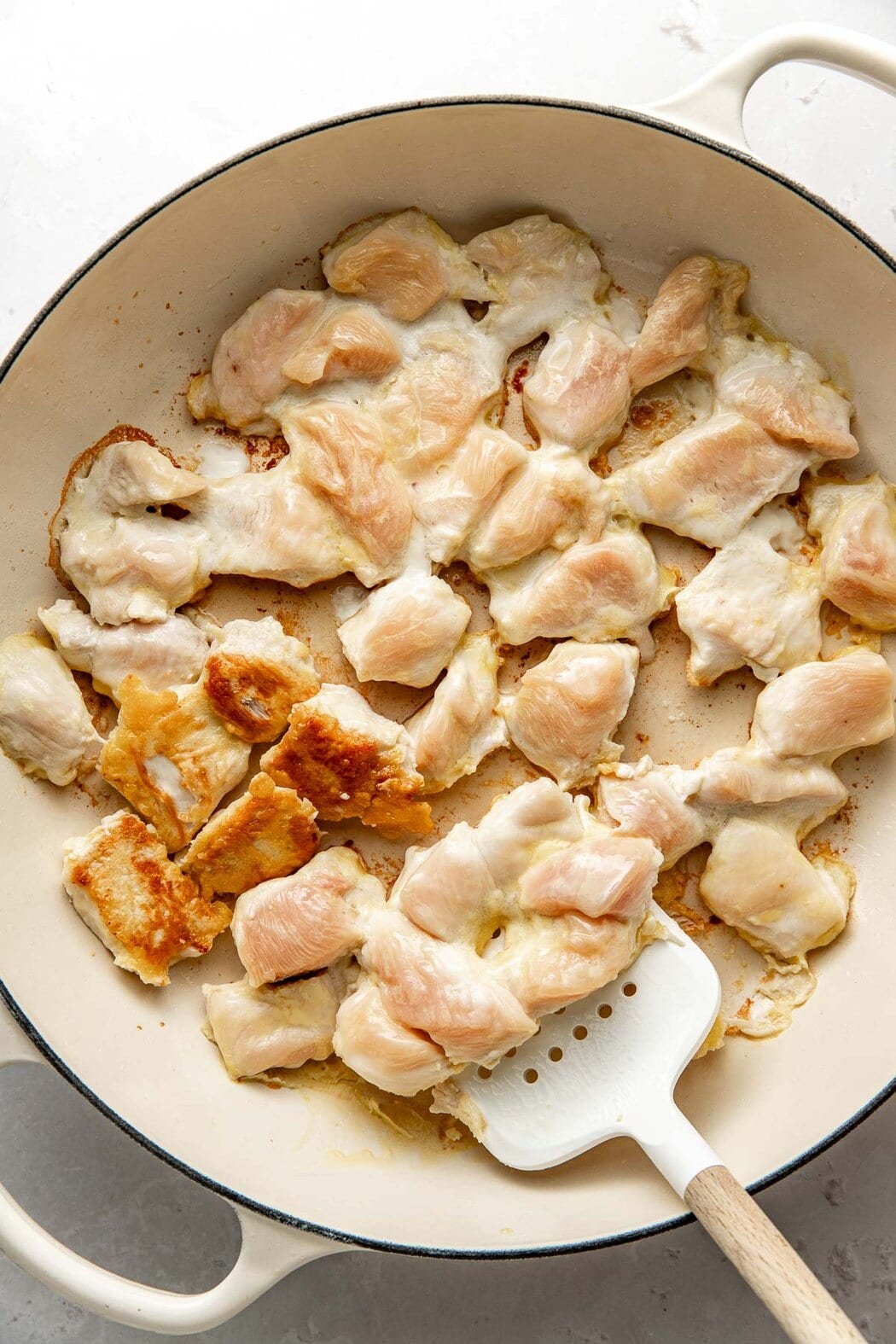 Overhead view of a skillet filled with pieces of chicken browning. 