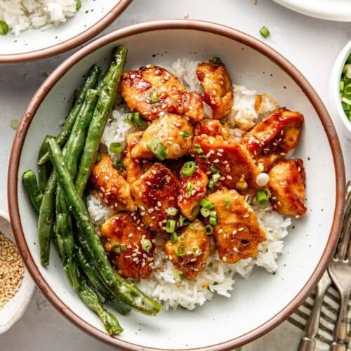 Overhead view of a plate filled with white rice, sesame chicken pieces, and roasted green beans.