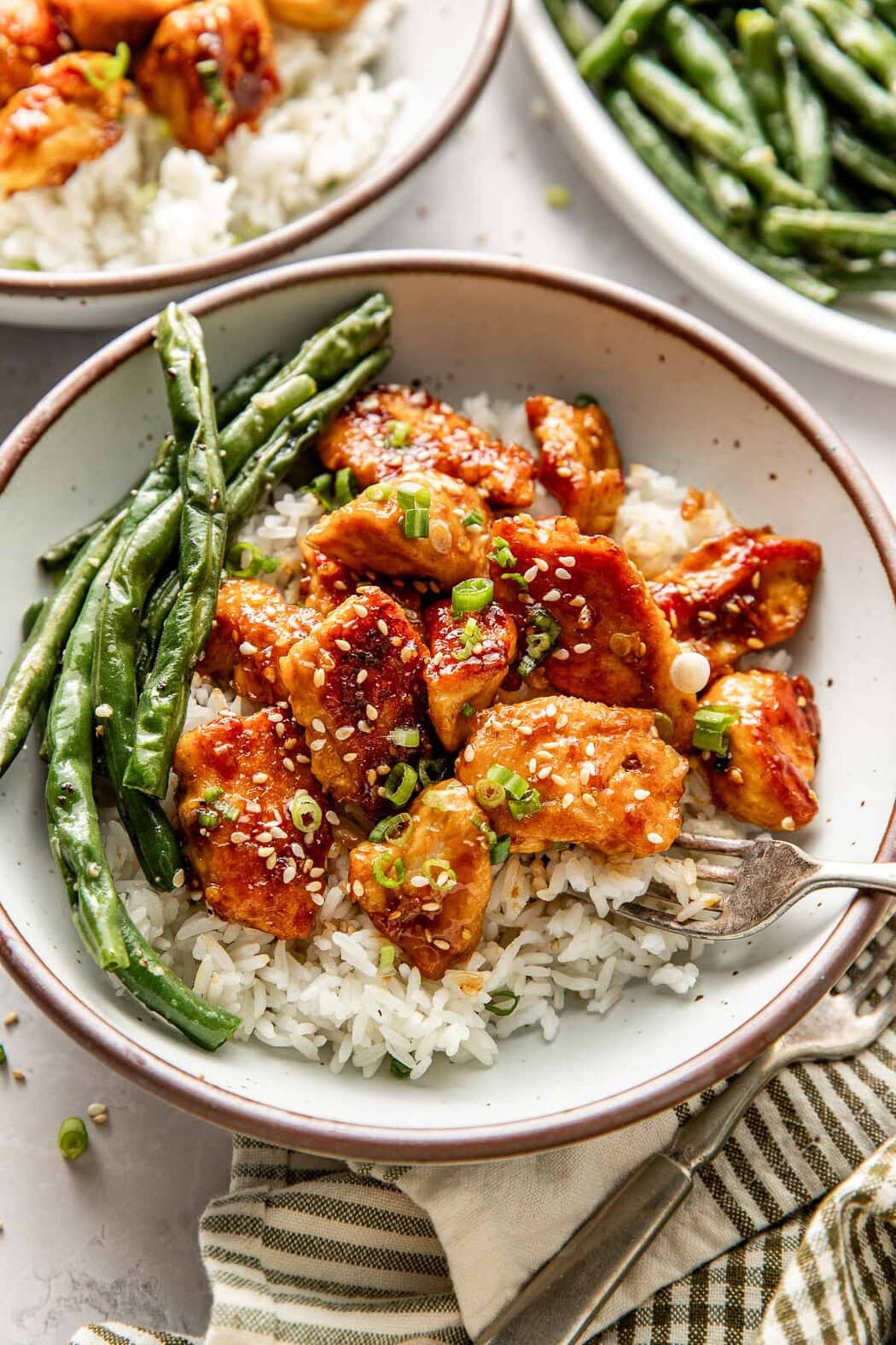 Close up view of a plate filled with rice and sesame chicken next to freshly roasted green beans. 