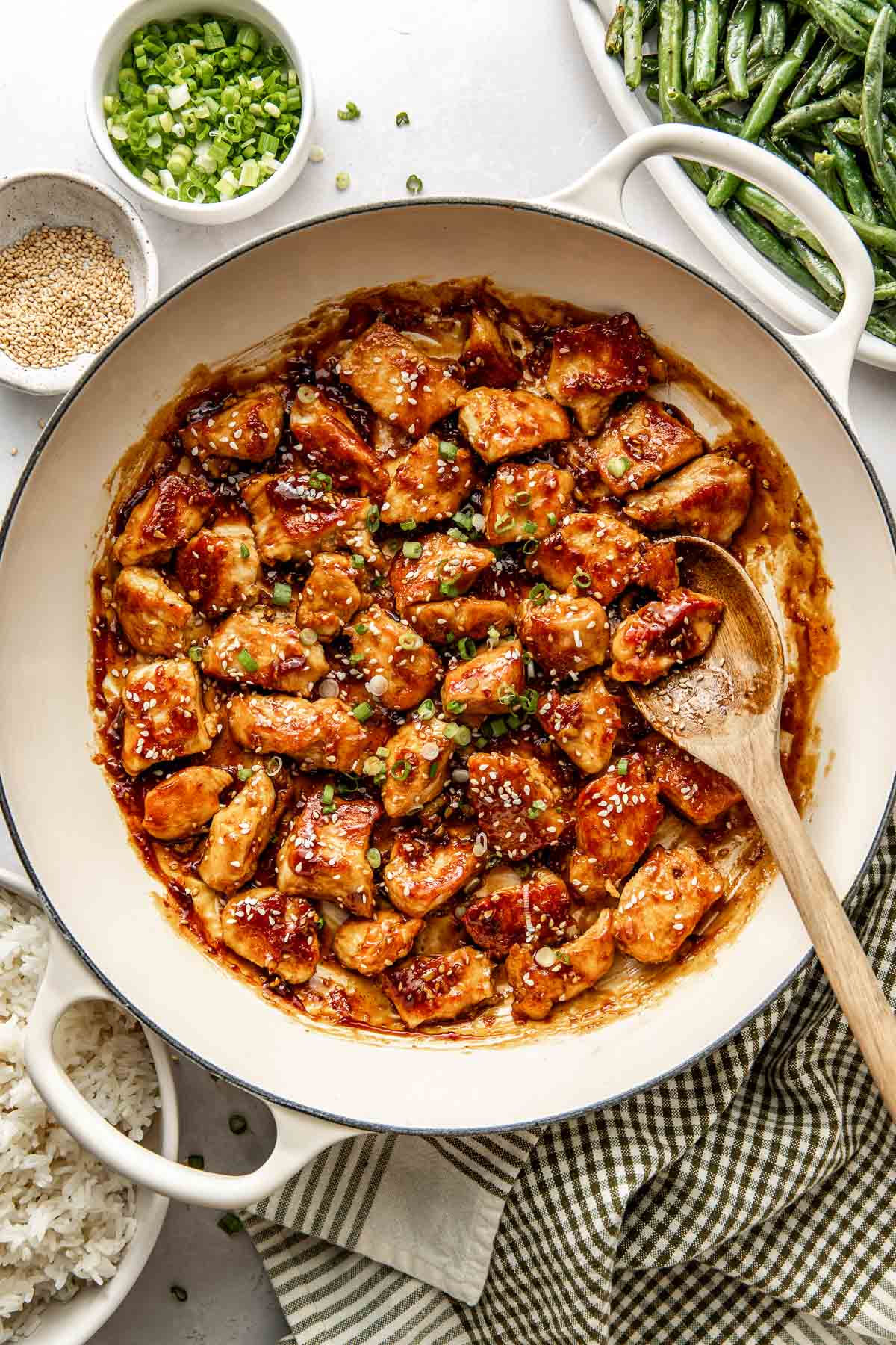 Overhead view of a skillet of sesame chicken in sauce and topped with sesame seeds and green onions. 