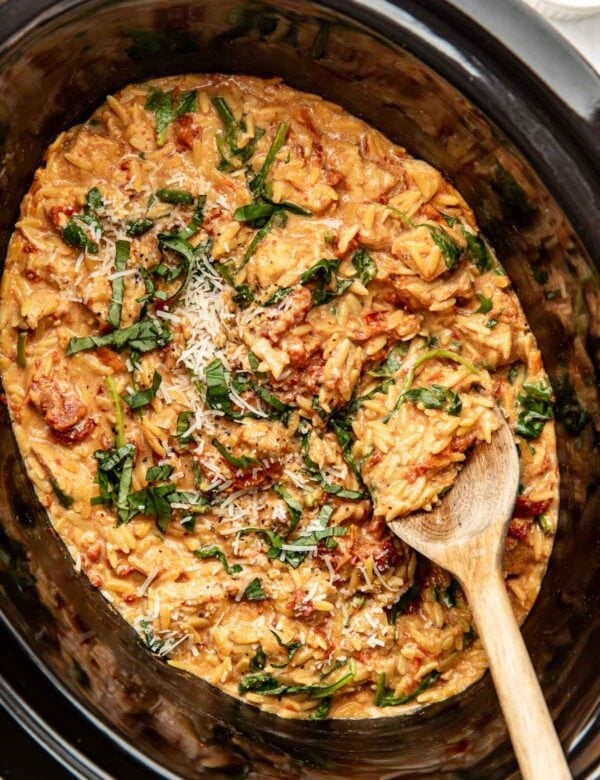 Overhead view of a slow cooker filled with creamy chicken and orzo topped with fresh basil and parmesan cheese.