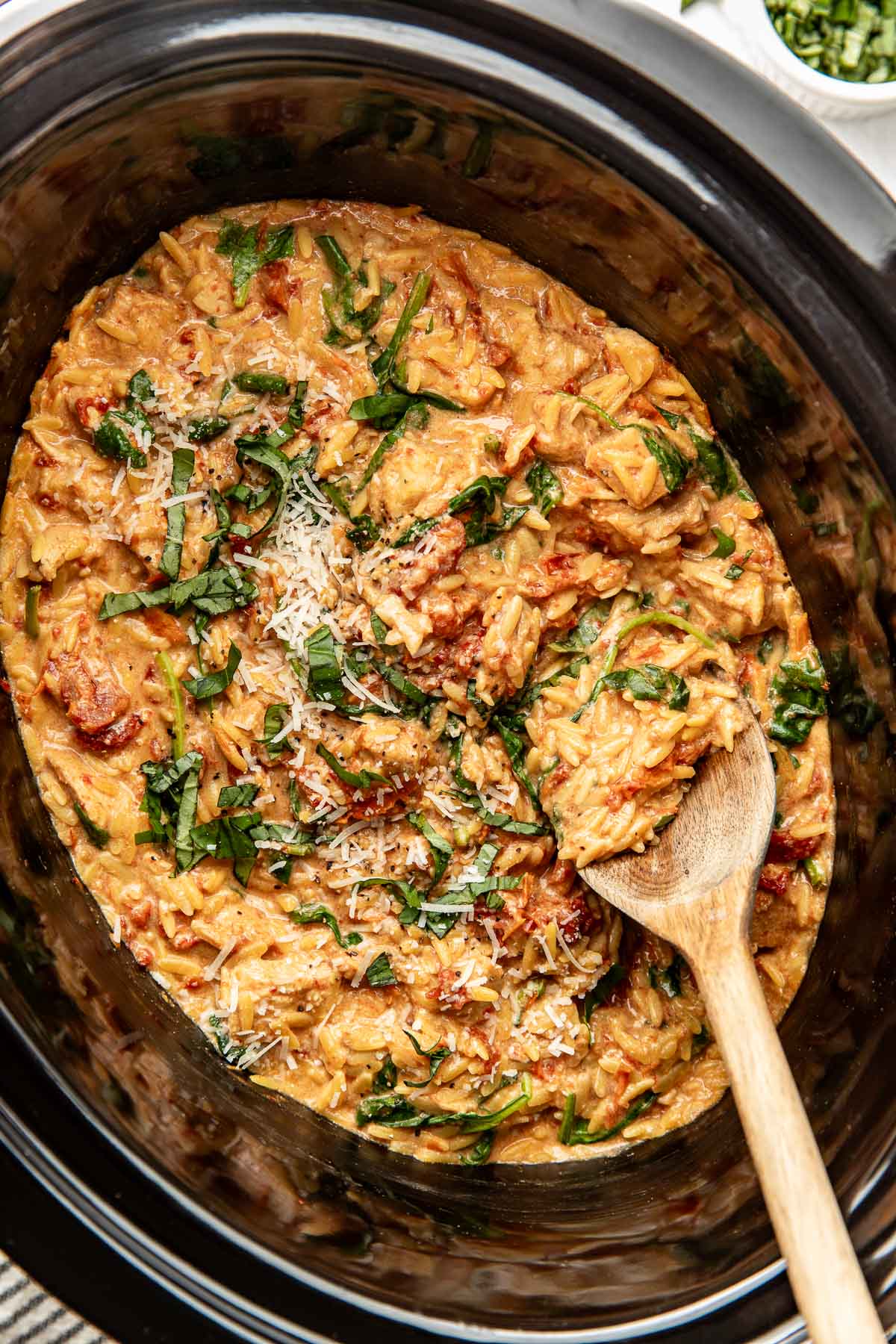 Overhead view of a slow cooker filled with Tuscan Chicken with Orzo and topped with fresh basil and shredded parmesan cheese. 