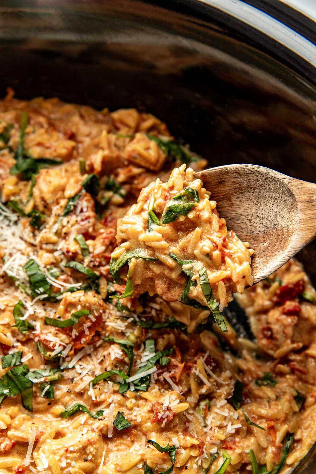 Close up view of a wooden spoon scooping out a spoonful of Crockpot Tuscan Chicken with Orzo showing the creamy texture. 