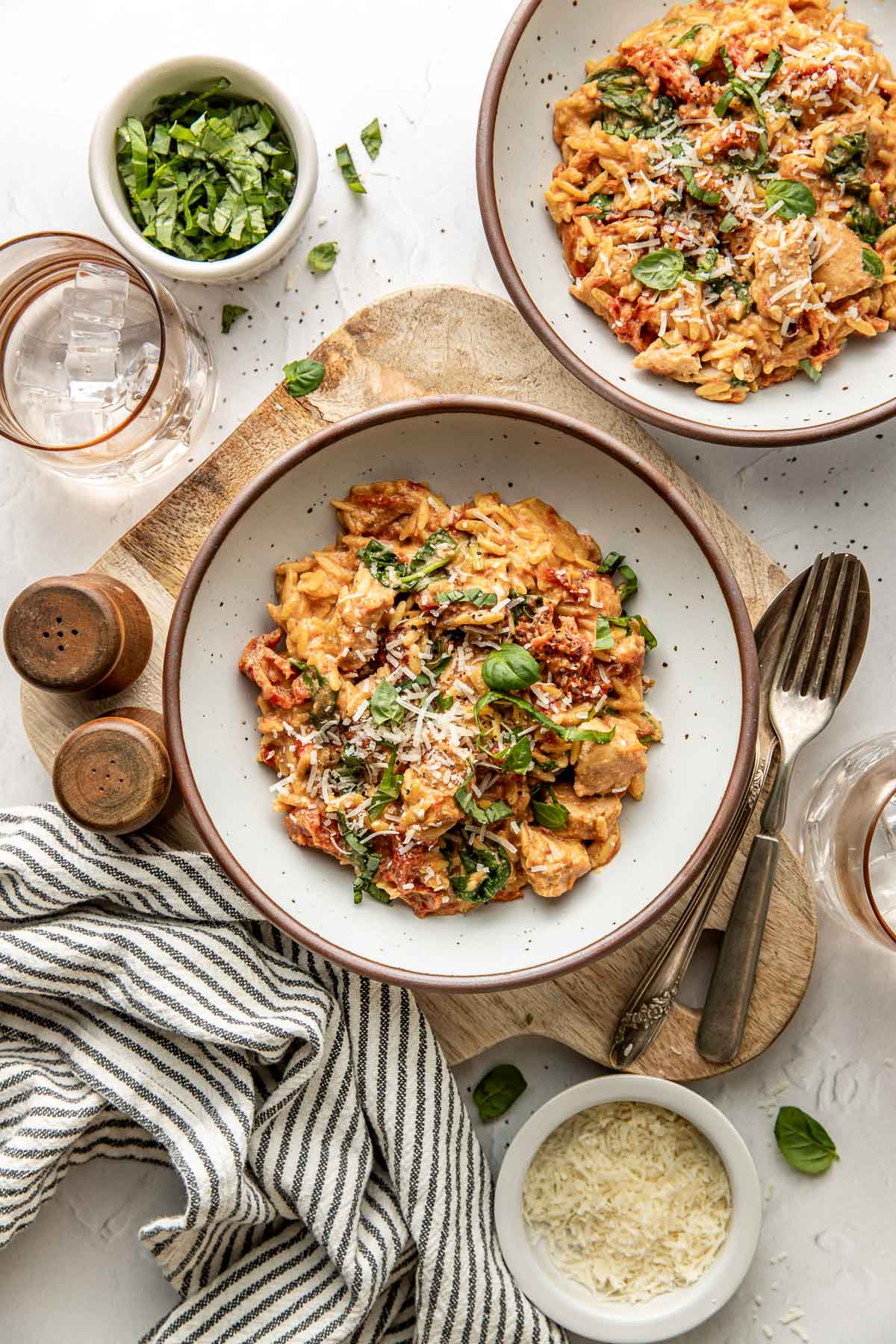 Overhead view of a marble white countertop with two ceramic bowls of Crockpot Tuscan Chicken with Orzo topped with fresh basil and shredded parmesan cheese. 