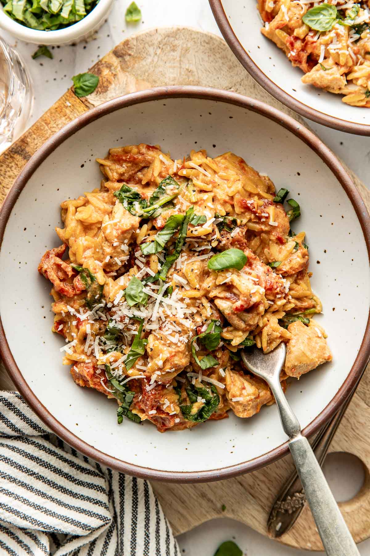 Overhead view of a white ceramic plate filled with Crockpot Tuscan Chicken with Orzo topped with fresh basil and shredded parmesan cheese. 