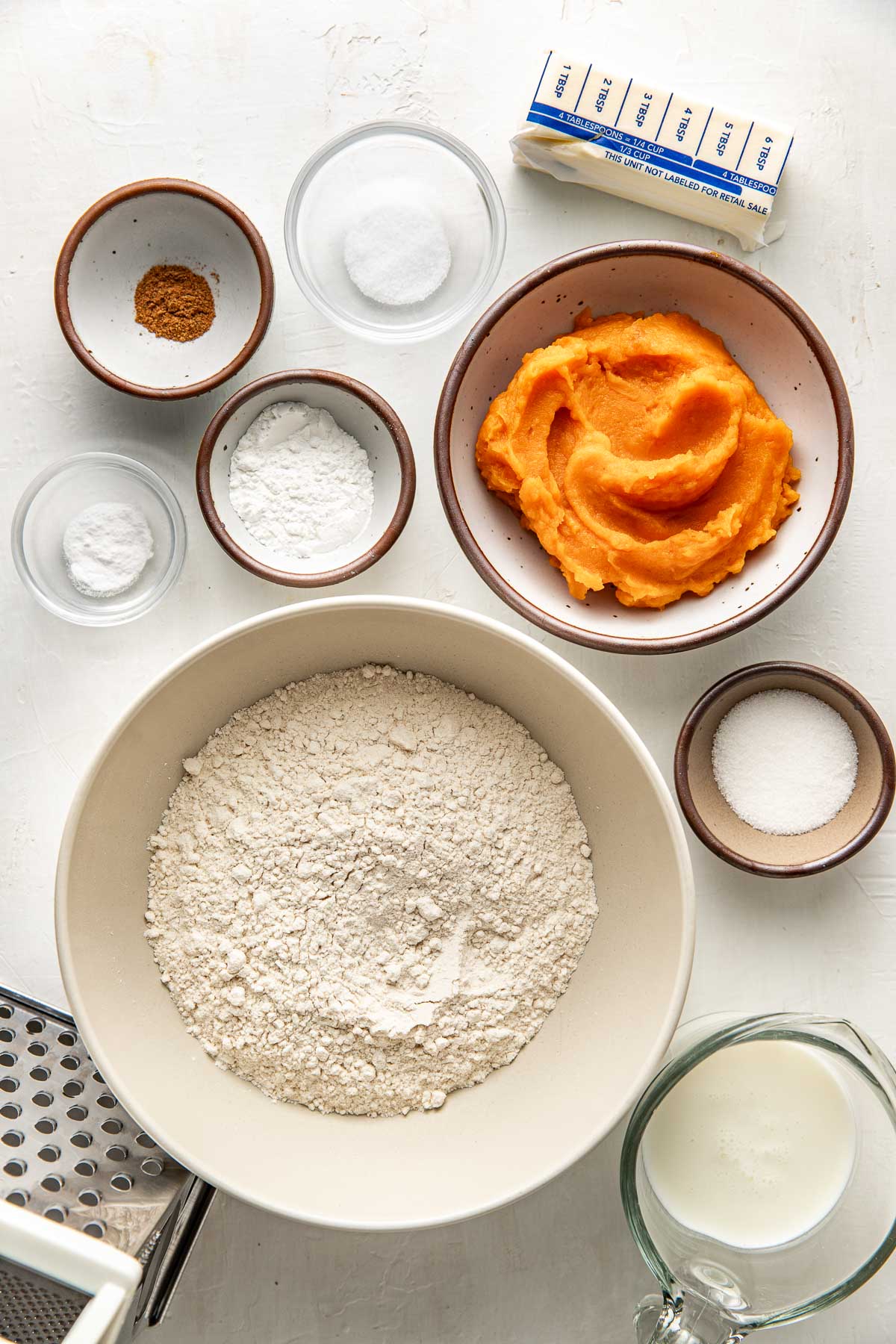 Ingredients to make homemade sweet potato biscuits arranged on a white surface alongside a box grater.