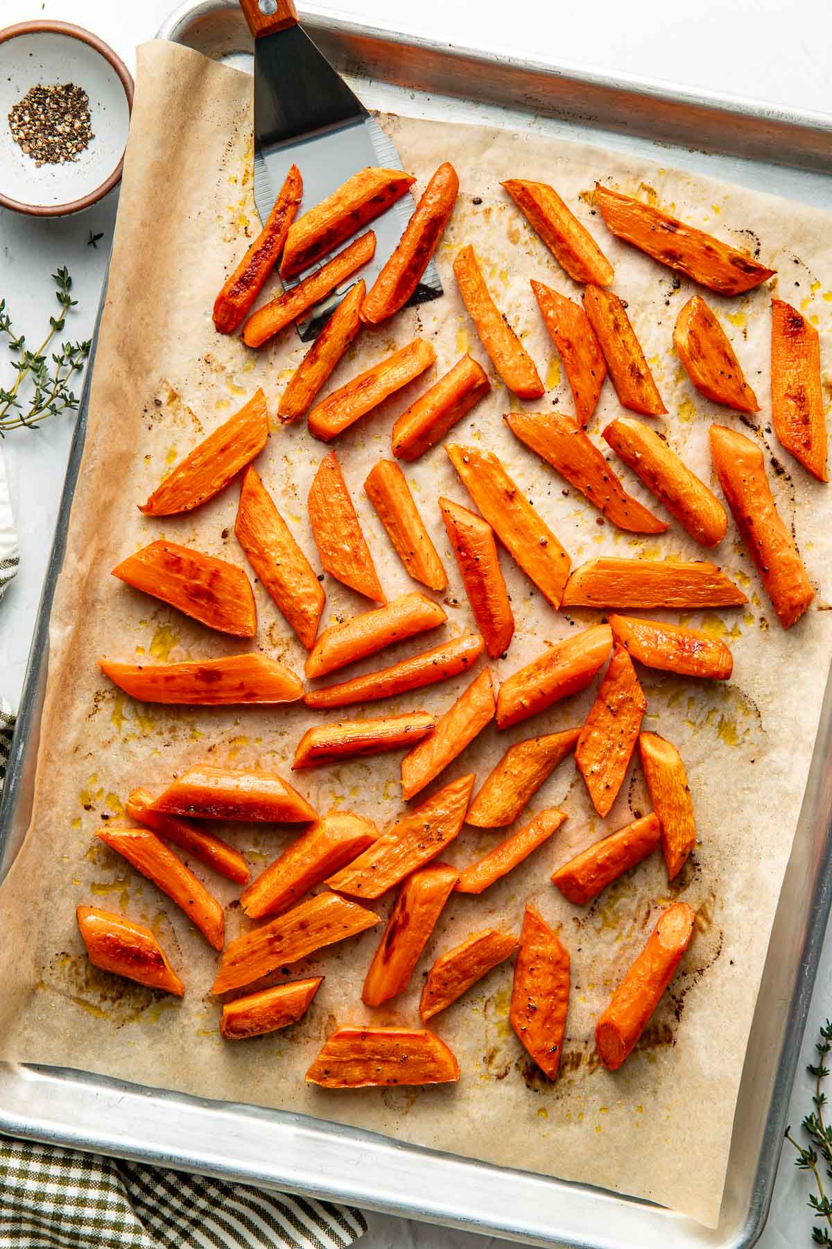 Overhead view of a sheet pan lined with parchment paper and filled with freshly roasted carrots topped with seasonings.