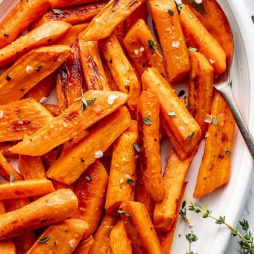 Overhead view of a platter filled with freshly roasted carrots topped with fresh herbs and black pepper.