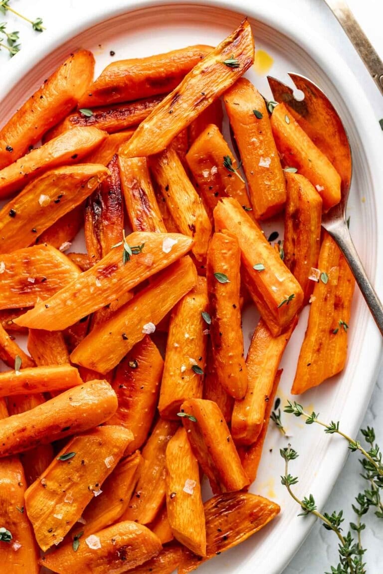 Overhead view of a platter of roasted carrots garnished with flaked sea salt and fresh thyme. 
