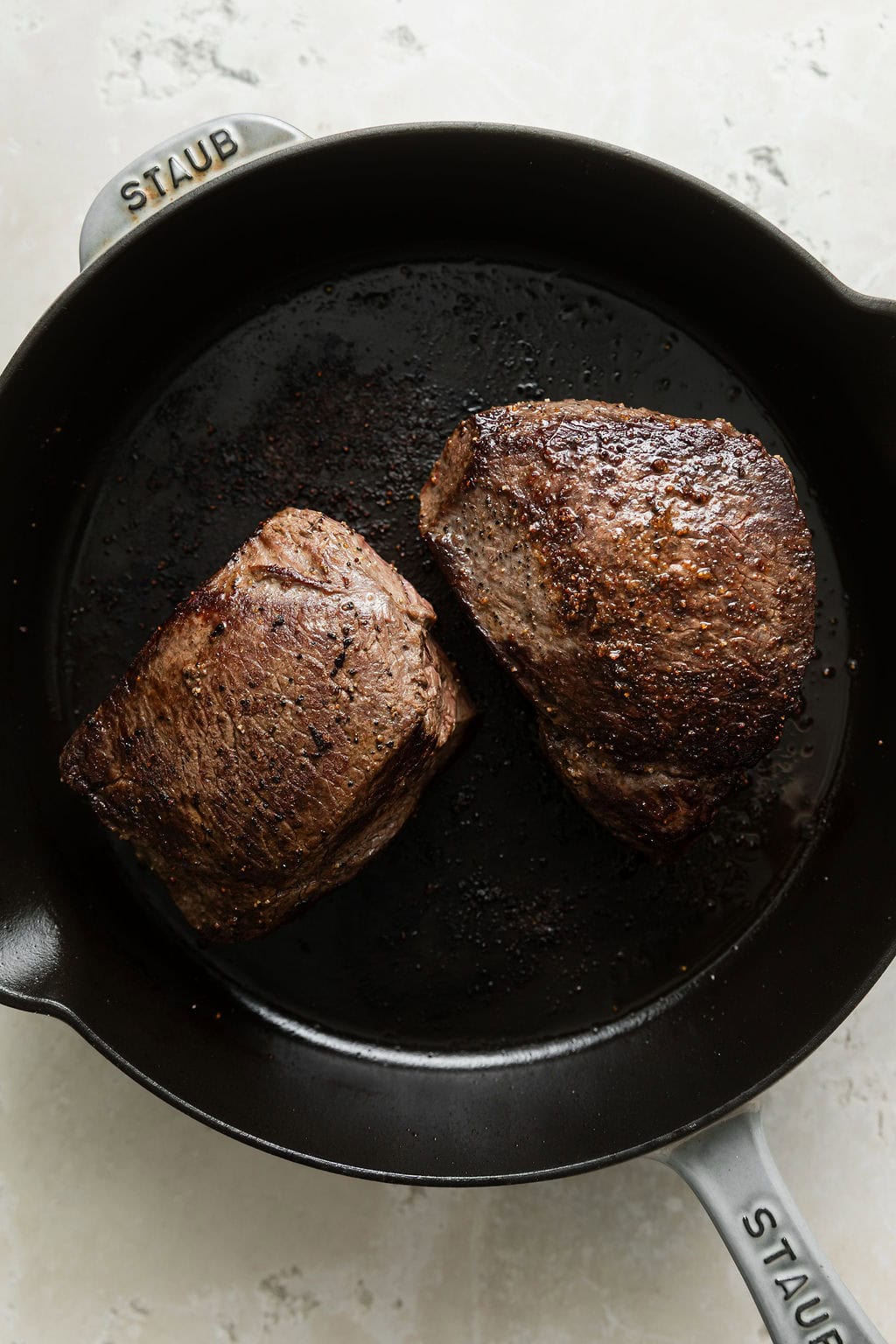 Close up view of two seared and seasoned venison roasts in a black cast iron pan. 