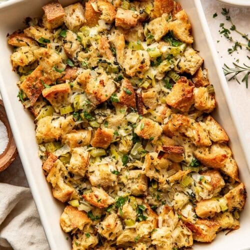 Overhead view of a white baking dish filled with stuffing topped with fresh herbs.