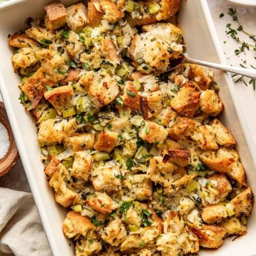 Overhead view of a white baking dish filled with freshly roasted stuffing with herbs sprinkled on top.