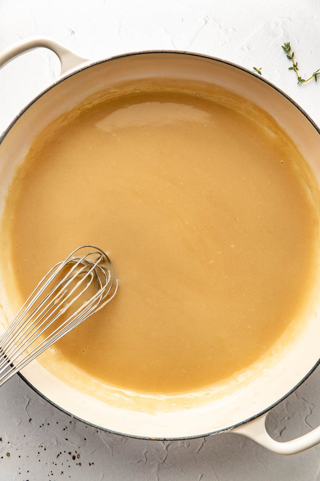 Overhead view of a white skillet filled with Turkey Gravy being whisked with a wire whisk. 