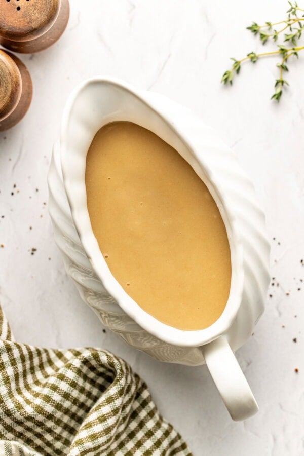 Overhead view of a white gravy boat filled with turkey gravy on a marble countertop with a plaid towel on the side.